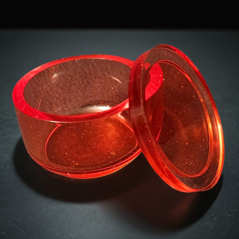 Rotes rundes Döschen aus transparentem, glitzerndem Harz.
