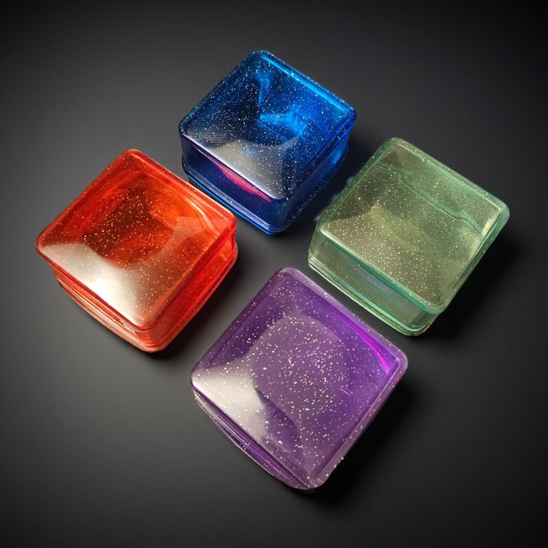 Vier quadratische Dosen mit Deckel aus glitzerndem, transparentem Harz – in den Farben Blau, Lila, Rot und Mintgrün