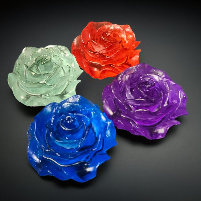 Vier handgefertigte Rosen aus glitzerndem Harz in Blau, Lila, Rot und Mintgrün auf dunklem Untergrund.