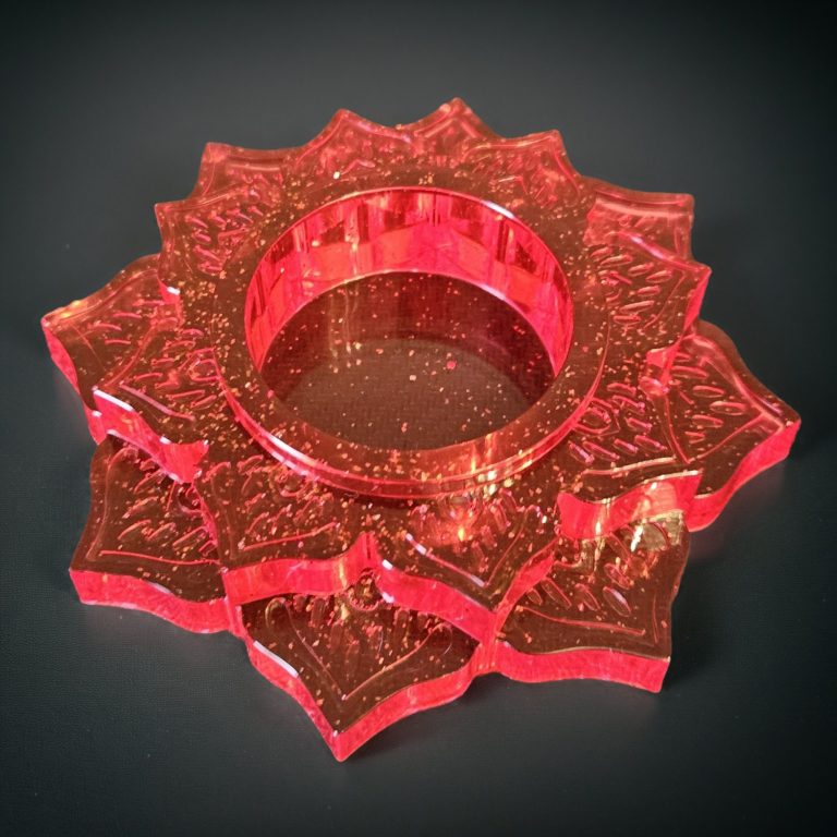 Roter handgegossene Teelichthalter in stufiger Blütenform mit feinen Ornamentstrukturen aus transparentem Harz mit Glitzer.