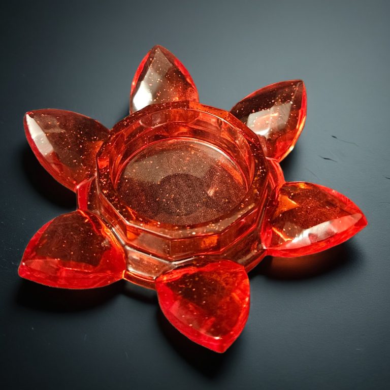 Roter Teelichthalter aus Resin in Blumenform mit fächerartig angeordneten Blütenblättern – transparent mit Glitzereffekt.