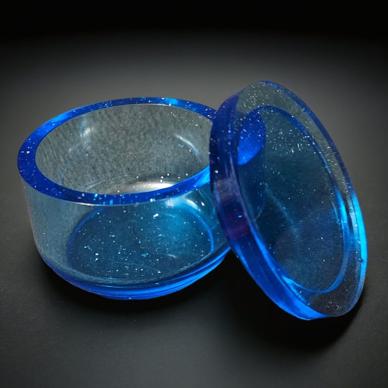 Blaues rundes Döschen aus transparentem, glitzerndem Harz.
