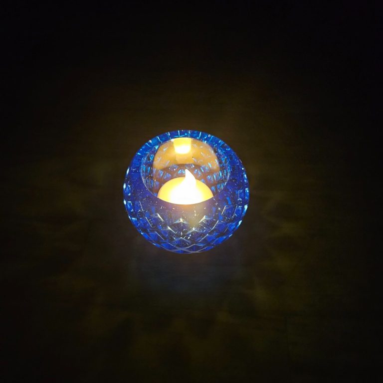 Blauer kugelförmiger Teelichthalter mit Rautenmuster aus transparentem Harz mit feinem Glitzereffekt.