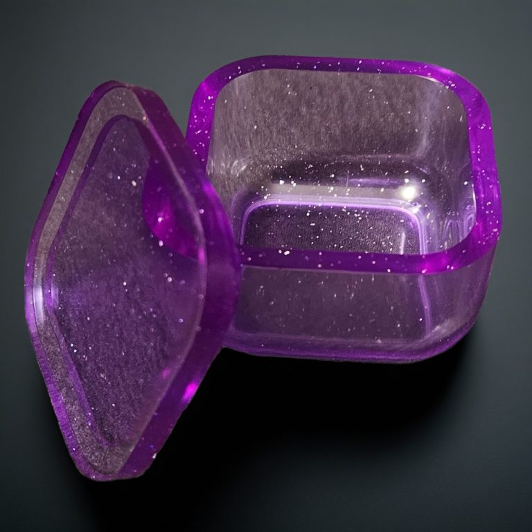 Lila, viereckiges kleines Kästchen aus transparentem, glitzerndem Harz.